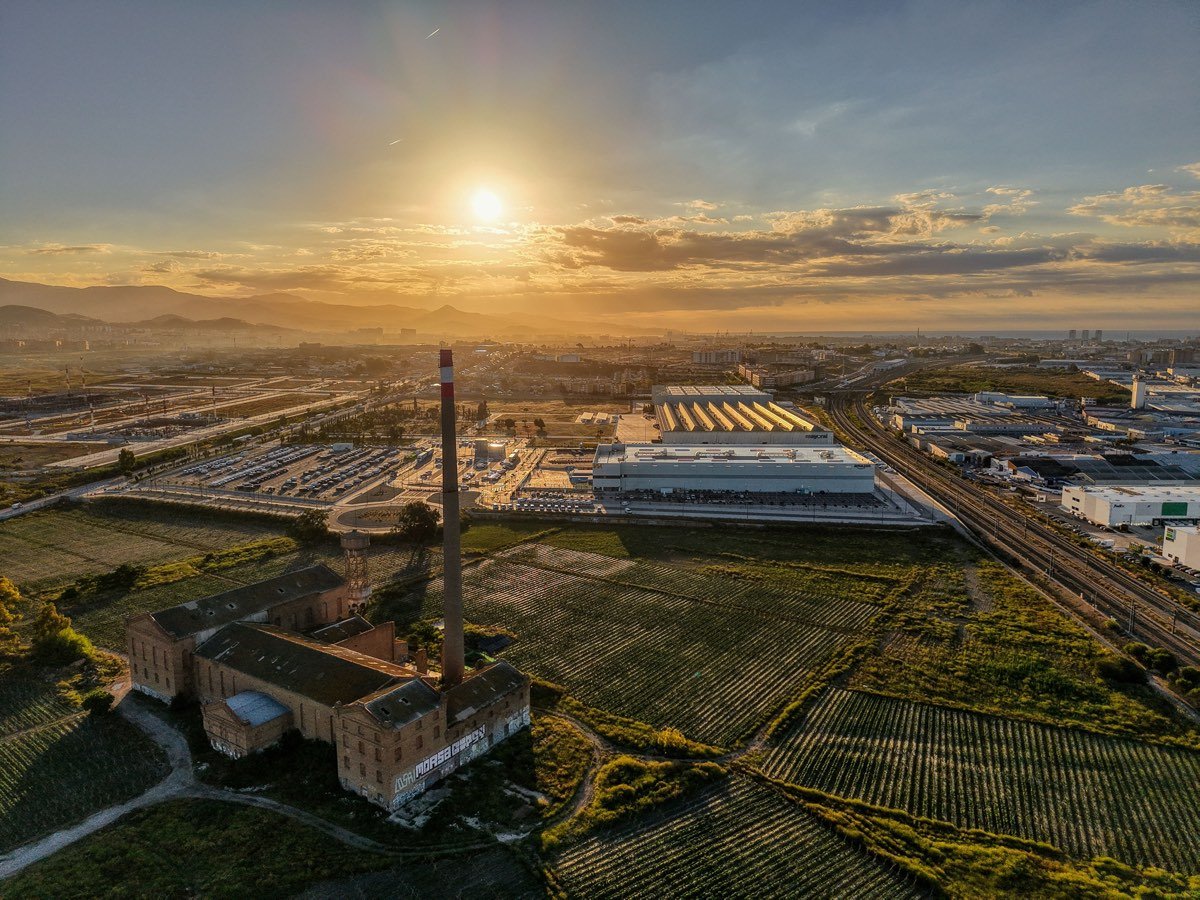 Vista aérea de una zona industrial con chimenea y campos de cultivo al atardecer